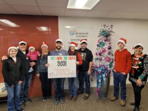 Koox dhoola cadeynaya oo xidhan koofiyadaha Santa ayaa taagan qol iftiimaya oo sita calaamad ay ku qoran tahay "2023 OHVA Toy Drive 9,091 TOYS" oo ay weheliyaan geed kirismas oo farxad leh oo lagu qurxiyey casaan iyo buluug.